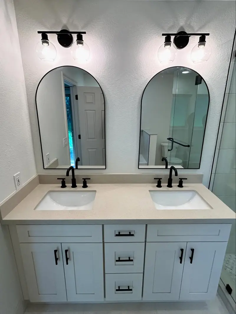 Modern double sink bathroom vanity with arched mirrors, wall sconces, white countertop, and light gray cabinets.