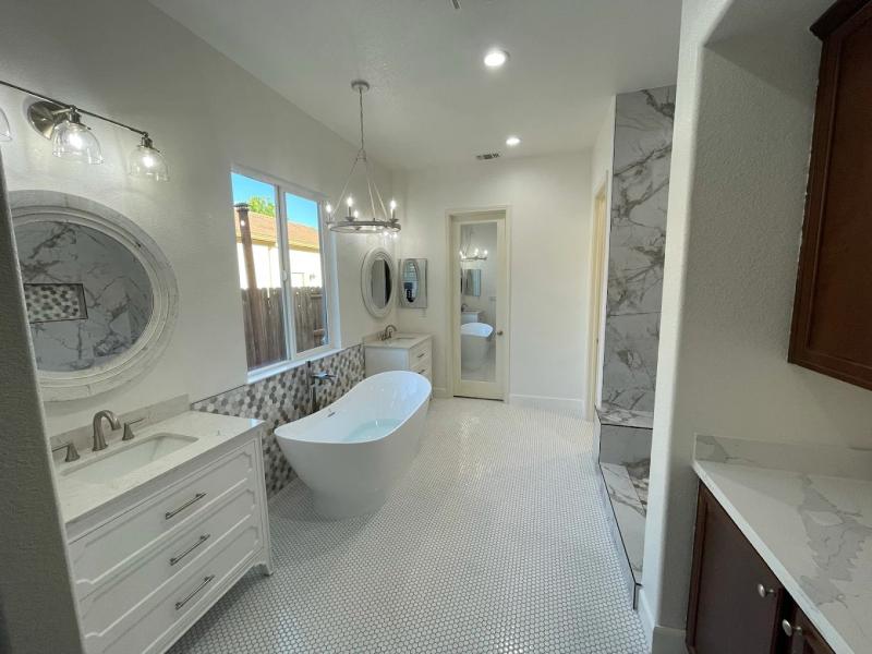 Luxury bathroom remodeling with a freestanding soaking tub, white double vanity, marble shower walls, custom tile flooring, and modern lighting.